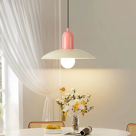 Pink pendant light hanging above a table with a vase of flowers and fruit.