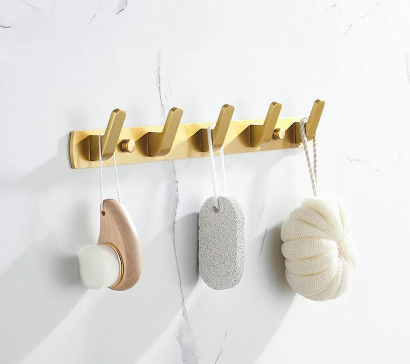 Gold wall hook with various bath items on a white background