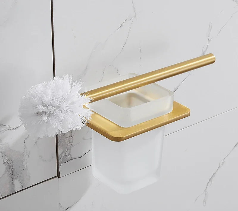 Gold toilet brush holder with a white toilet brush against a tiled bathroom wall.