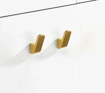Two gold wall hooks on a white wall.