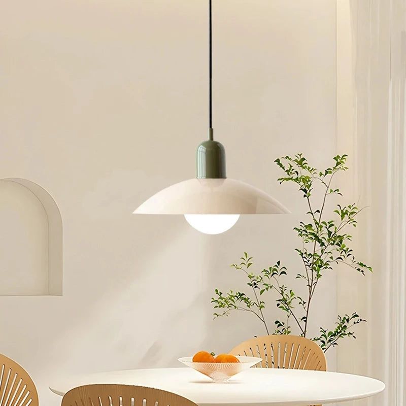 Modern pendant light hanging above a dining table with a plant in the background