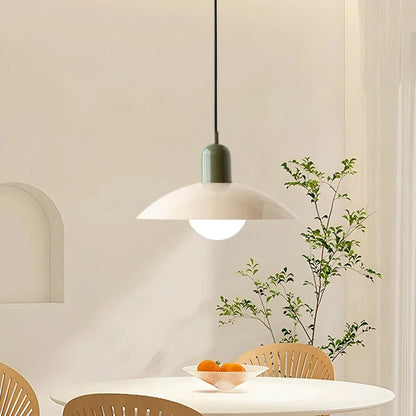 Modern pendant light hanging above a dining table with a plant in the background
