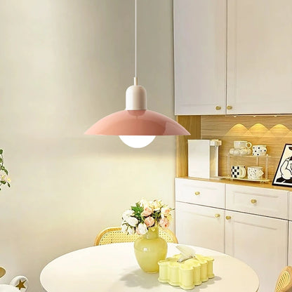 Modern kitchen with a pink pendant light, white cabinets, and decorative items on a table.