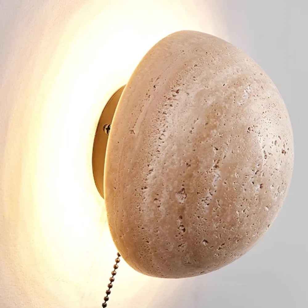 Round stone-like wall sconce with a gold fixture on a light gray background