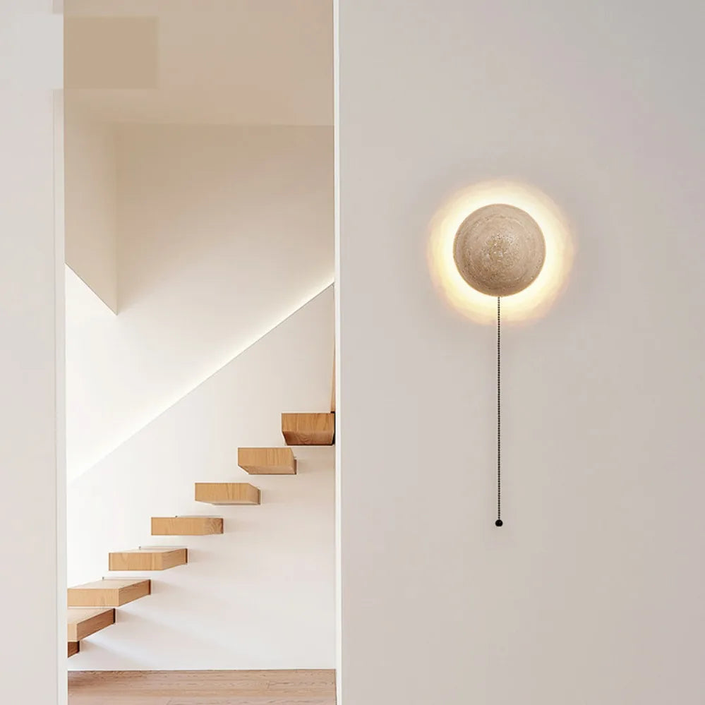 Modern wall lamp with round light fixture on a white wall next to a staircase.