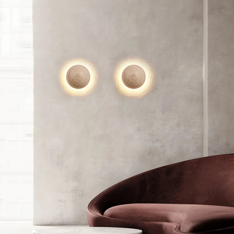 Two round wall lights on a textured wall with a brown sofa in the foreground.