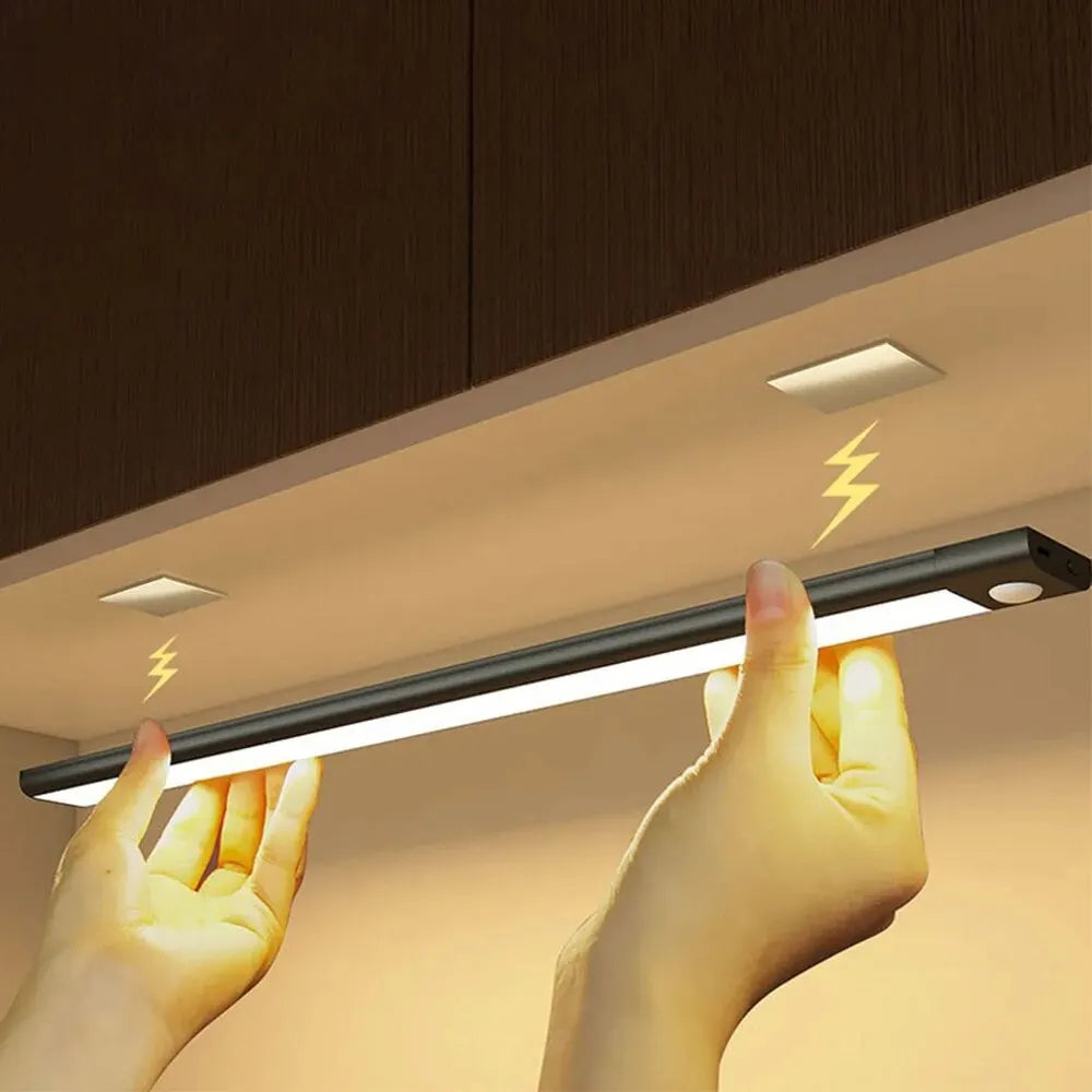 Under-cabinet LED light bar being held by a hand with a wooden cabinet background